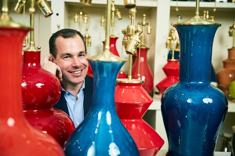 Christopher Spitzmiller surrounded by red and blue lamps he has made by hand.