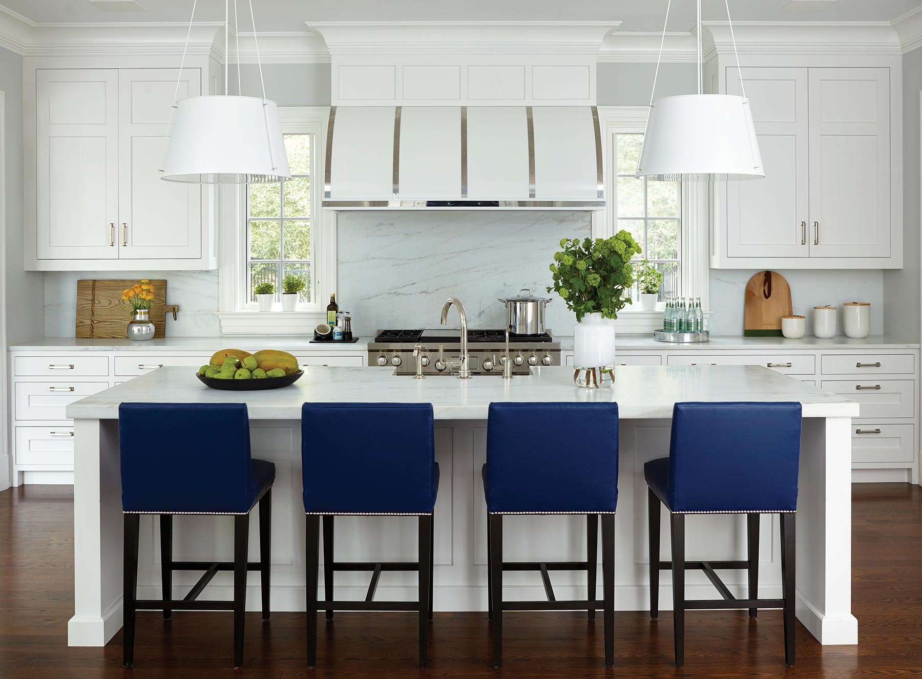 A white kitchen island and stove with a pop of color in the line of blue barstools in front