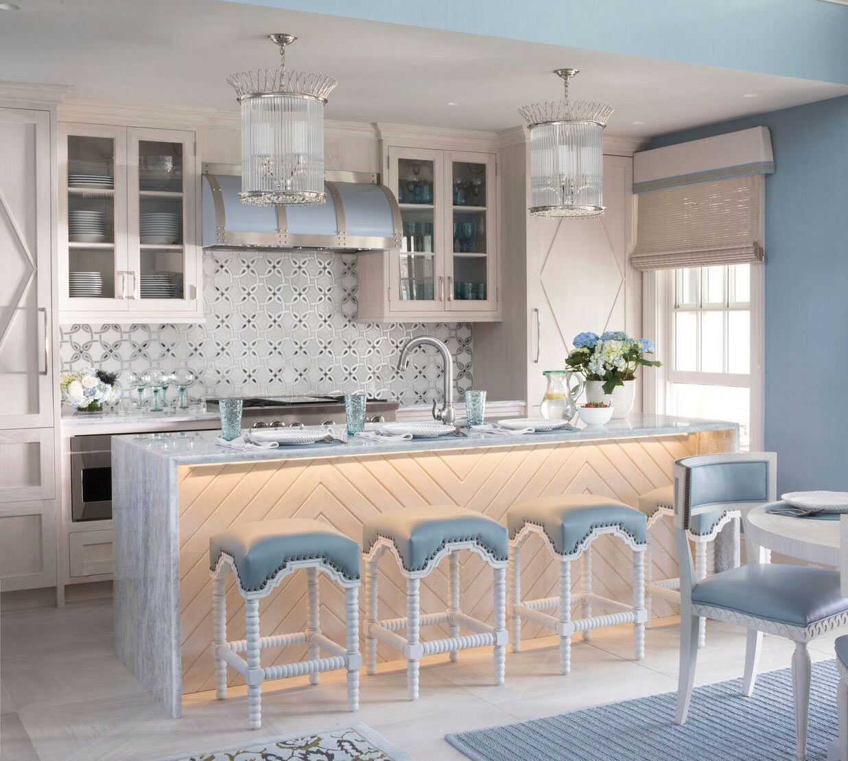 A luxurious light blue kitchen island with cloud blue seats, blue stove hood and other accents