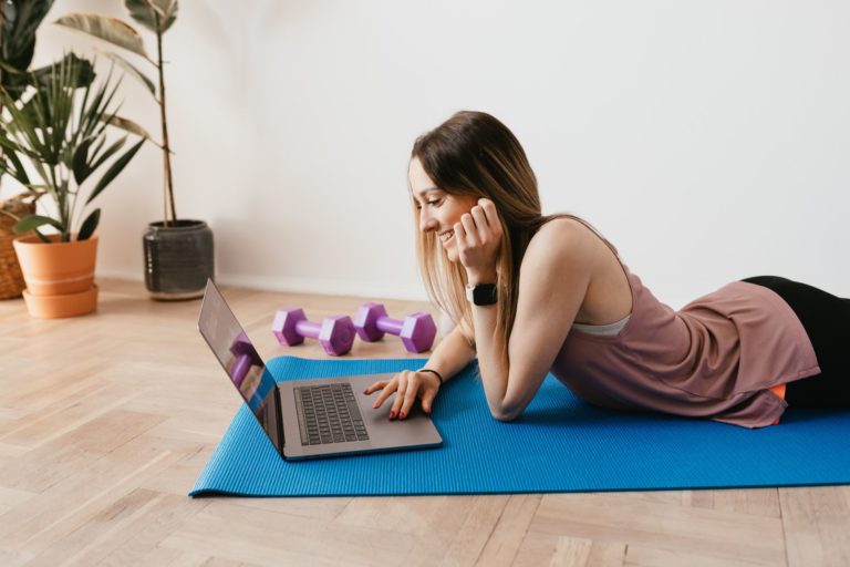 women laying on yoga mat on laptop